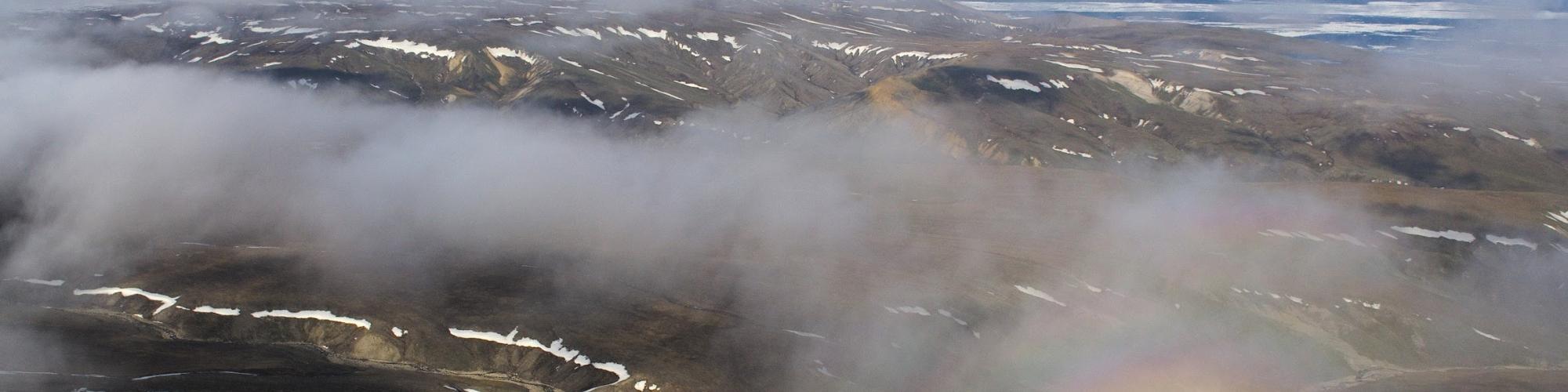 Survol de montagnes et nuages, avec arc-en-ciel